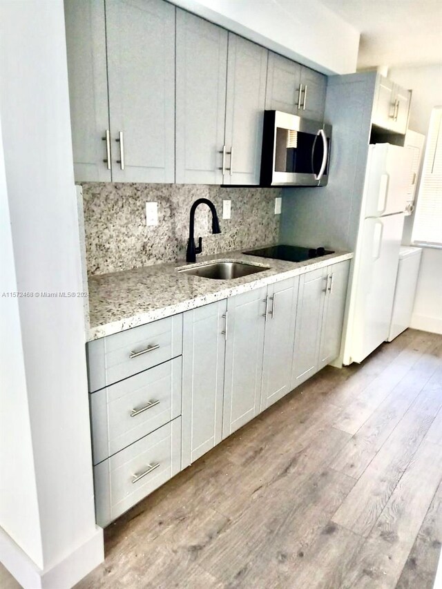 kitchen featuring light stone countertops, light wood-type flooring, white refrigerator, gray cabinets, and sink