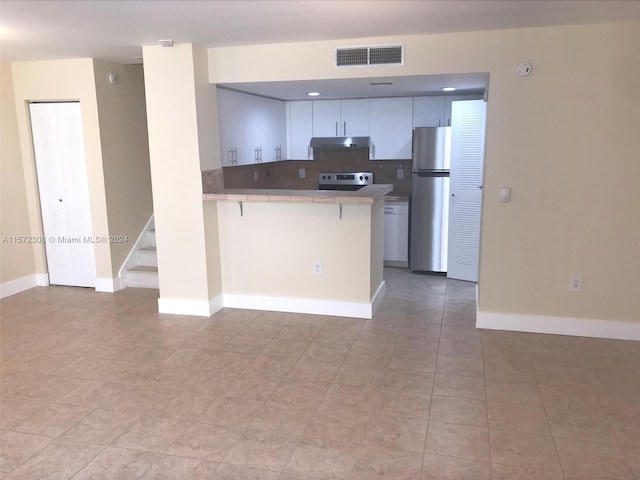 kitchen with stainless steel refrigerator, a kitchen breakfast bar, kitchen peninsula, white cabinets, and range