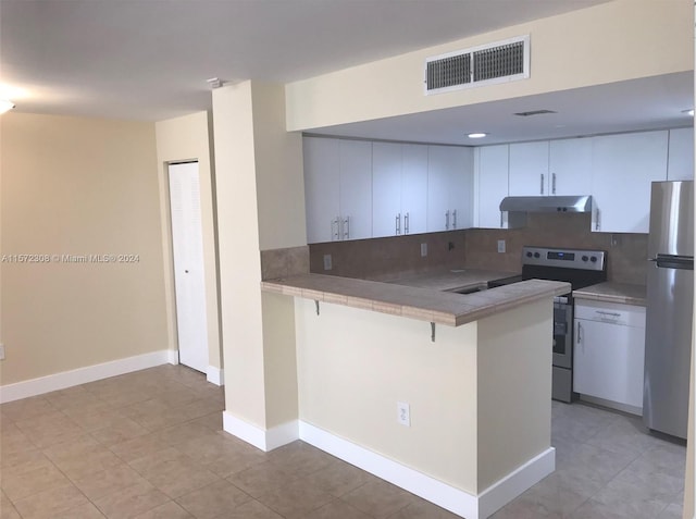 kitchen featuring kitchen peninsula, decorative backsplash, stainless steel appliances, white cabinets, and a breakfast bar area