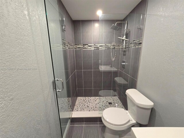 bathroom with a shower with shower door and toilet