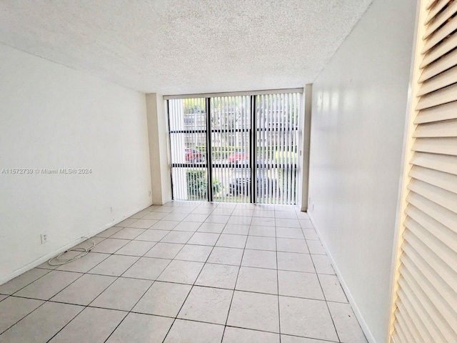 empty room with a textured ceiling, light tile flooring, and expansive windows