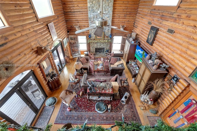 living room featuring a stone fireplace, hardwood / wood-style floors, ceiling fan, and rustic walls