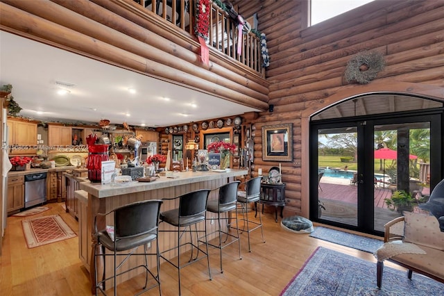 kitchen featuring light wood-type flooring, log walls, a breakfast bar area, french doors, and stainless steel dishwasher