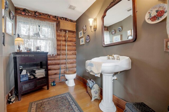 bathroom featuring hardwood / wood-style floors, log walls, and toilet