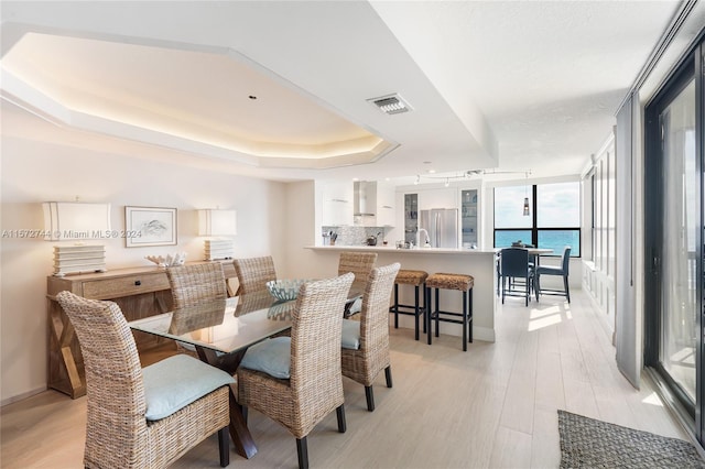 dining area featuring a water view, a tray ceiling, and light wood-type flooring