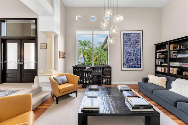 living room with french doors, light hardwood / wood-style floors, decorative columns, and a high ceiling