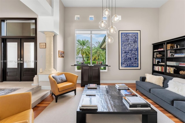 living room featuring french doors, light hardwood / wood-style flooring, ornate columns, and a towering ceiling