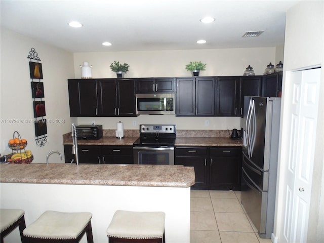 kitchen featuring sink, appliances with stainless steel finishes, light tile flooring, and a kitchen breakfast bar