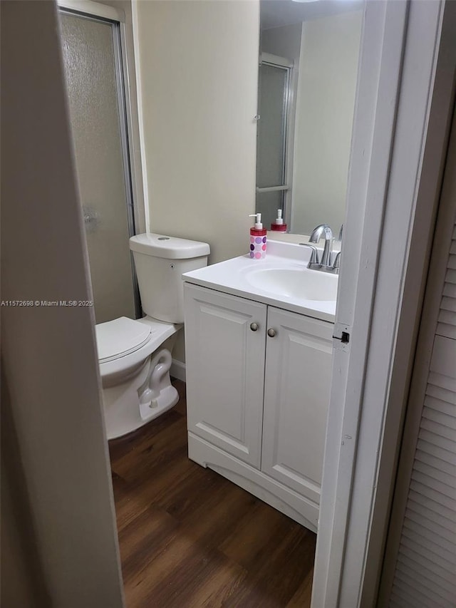 bathroom with wood-type flooring, vanity, toilet, and a shower with shower door