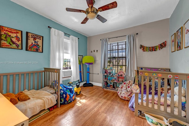 bedroom featuring light hardwood / wood-style flooring, ceiling fan, and a crib