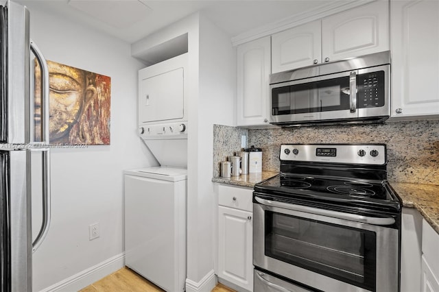 kitchen with appliances with stainless steel finishes, tasteful backsplash, dark stone counters, white cabinets, and stacked washer and dryer