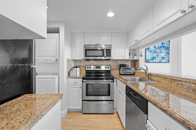 kitchen featuring sink, light stone countertops, appliances with stainless steel finishes, stacked washer / drying machine, and white cabinetry