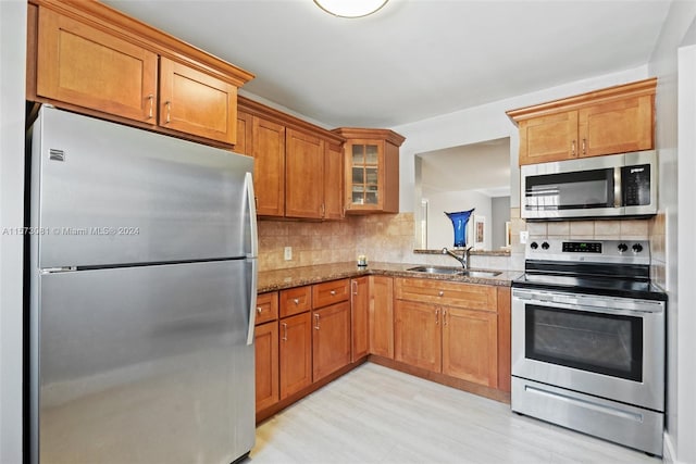 kitchen with sink, stone countertops, appliances with stainless steel finishes, light hardwood / wood-style floors, and decorative backsplash