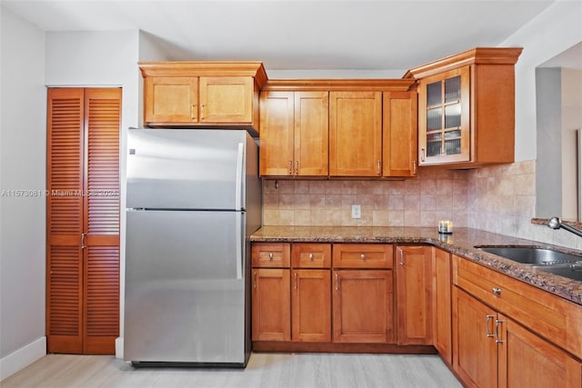 kitchen with light wood-type flooring, stainless steel fridge, stone counters, and decorative backsplash