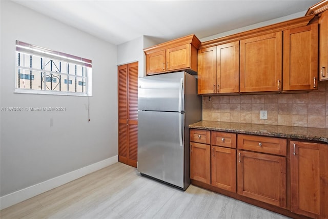 kitchen with dark stone counters, light wood-type flooring, stainless steel fridge, and tasteful backsplash