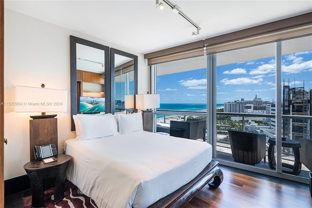 bedroom with access to exterior, dark hardwood / wood-style flooring, track lighting, floor to ceiling windows, and a water view