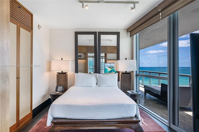 bedroom featuring rail lighting, a water view, and expansive windows