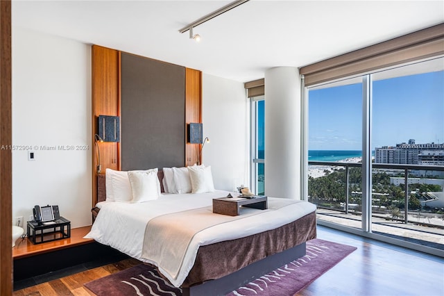 bedroom featuring access to exterior, a water view, track lighting, and dark wood-type flooring