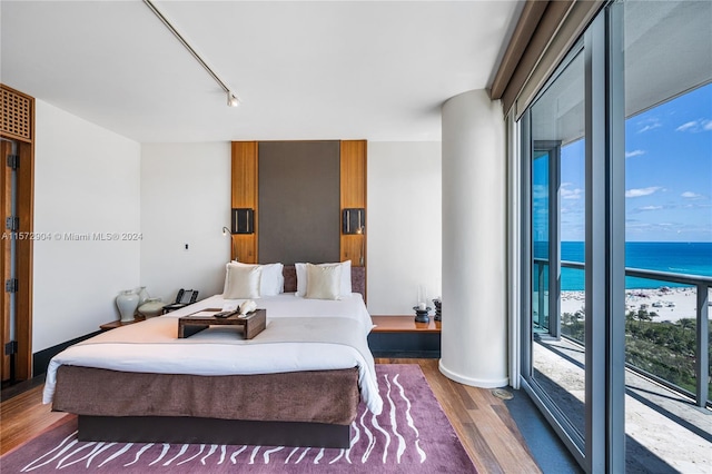 bedroom with a beach view, access to outside, a water view, and dark wood-type flooring