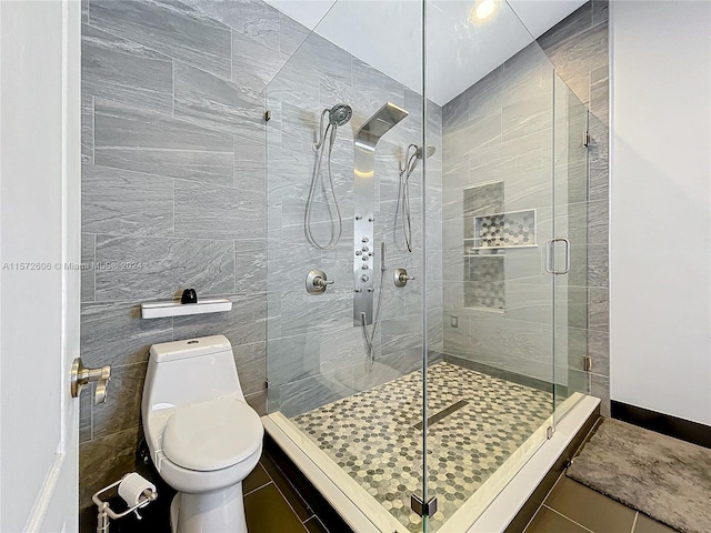 bathroom featuring tile patterned floors, a shower with door, tile walls, and toilet