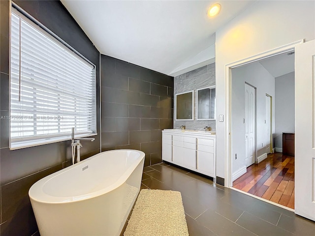 bathroom featuring a bathing tub, hardwood / wood-style floors, vaulted ceiling, vanity, and tile walls