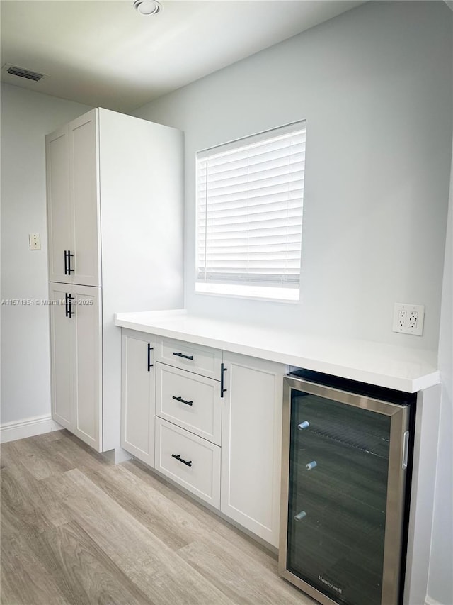 bar featuring wine cooler, light wood-style flooring, visible vents, and baseboards