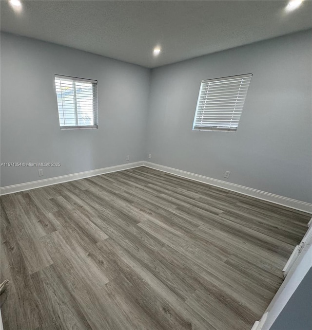 empty room featuring a textured ceiling, recessed lighting, wood finished floors, and baseboards