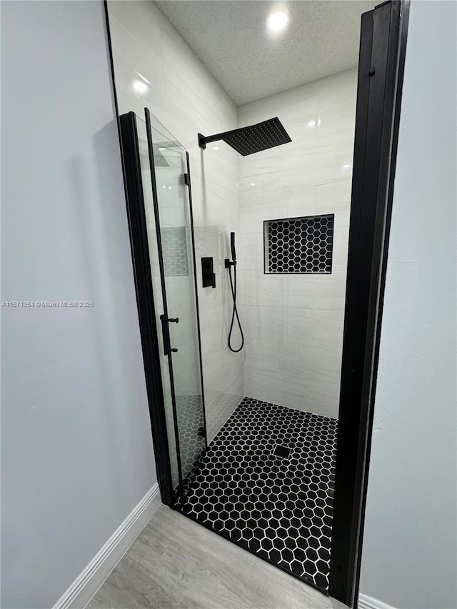 bathroom with a textured ceiling, a stall shower, wood finished floors, and baseboards