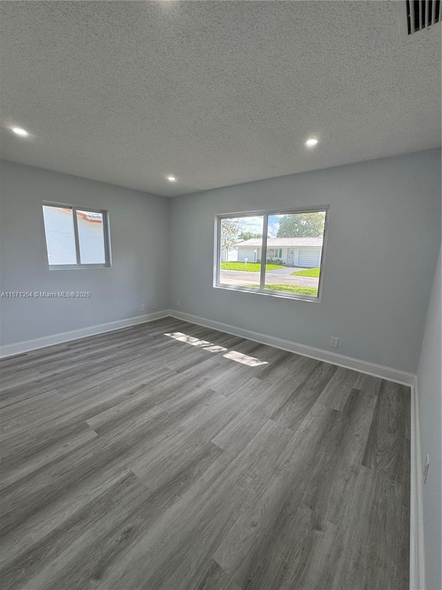 unfurnished room featuring visible vents, baseboards, dark wood-style flooring, a textured ceiling, and recessed lighting