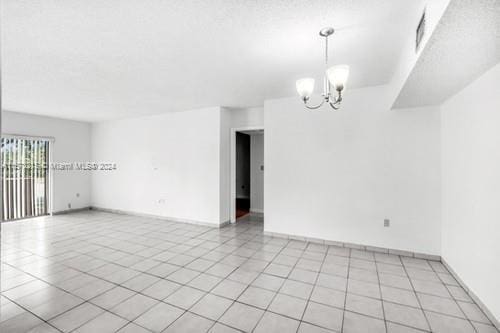 tiled empty room featuring an inviting chandelier