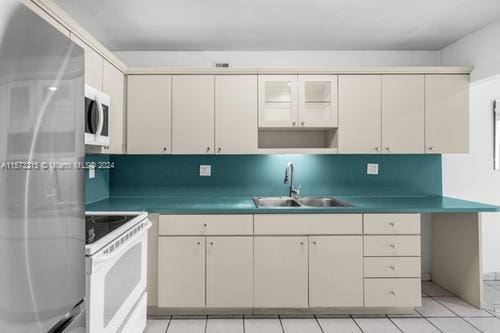 kitchen with appliances with stainless steel finishes, sink, backsplash, and cream cabinets