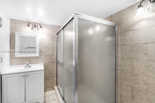 bathroom featuring vanity, tile patterned floors, a shower with door, and tile walls