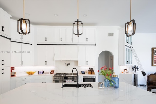 kitchen featuring range with two ovens, light stone counters, decorative light fixtures, and white cabinetry