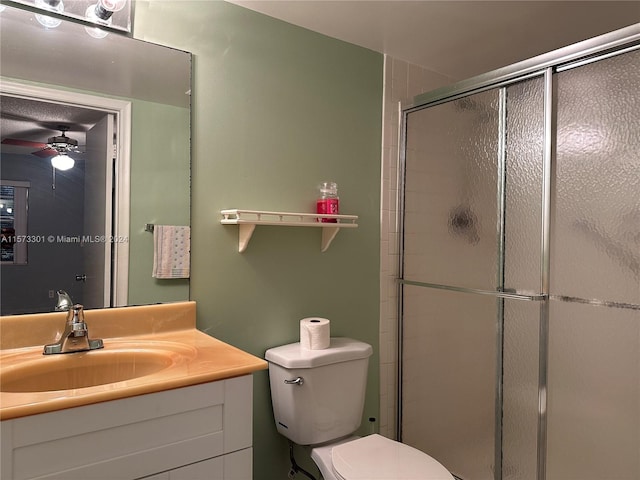 bathroom featuring vanity with extensive cabinet space, a shower with door, toilet, and ceiling fan