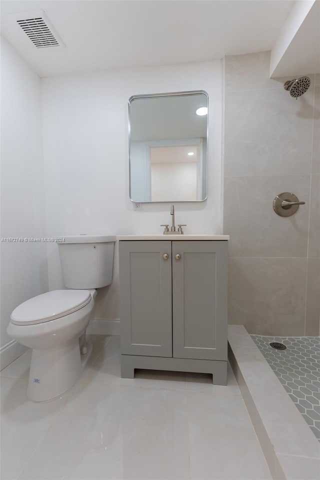 bathroom with a tile shower, toilet, tile patterned floors, and vanity