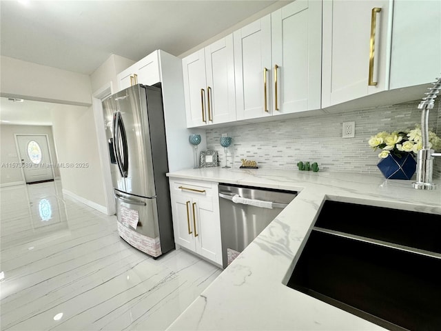 kitchen with light stone counters, white cabinets, decorative backsplash, and appliances with stainless steel finishes