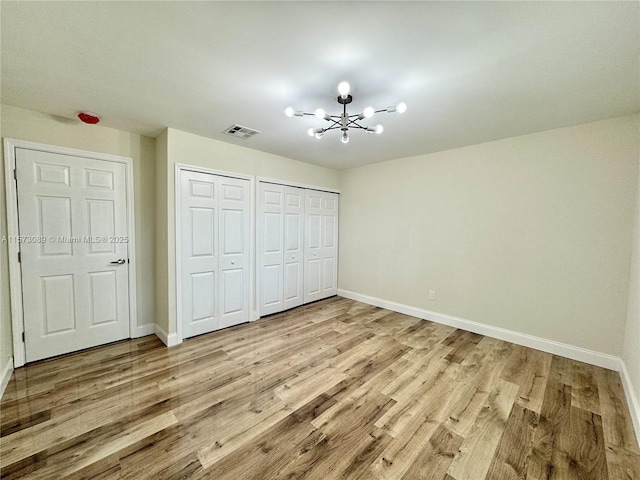 unfurnished bedroom with a chandelier, light hardwood / wood-style flooring, and two closets