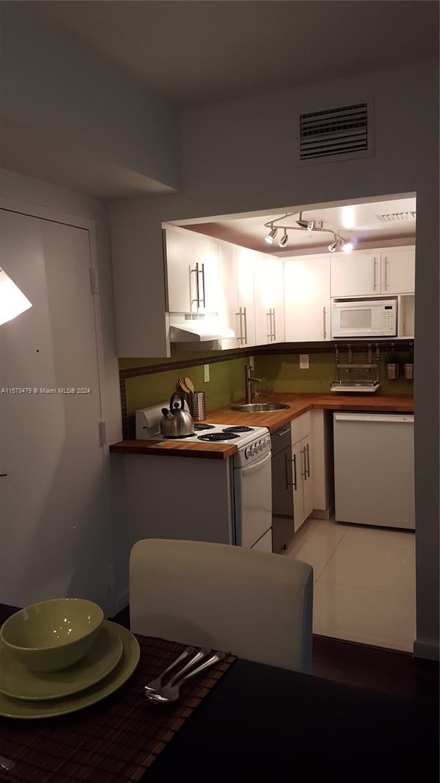 kitchen with white appliances, white cabinetry, backsplash, light tile floors, and sink