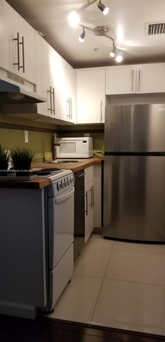 kitchen with white appliances, light tile flooring, rail lighting, and white cabinetry