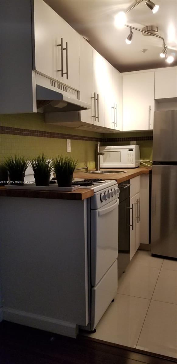 kitchen featuring white cabinetry, rail lighting, backsplash, light tile floors, and stainless steel fridge