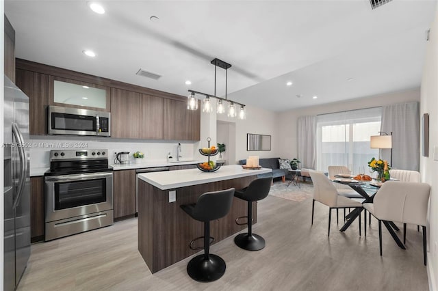 kitchen with decorative light fixtures, appliances with stainless steel finishes, light hardwood / wood-style floors, tasteful backsplash, and a kitchen breakfast bar