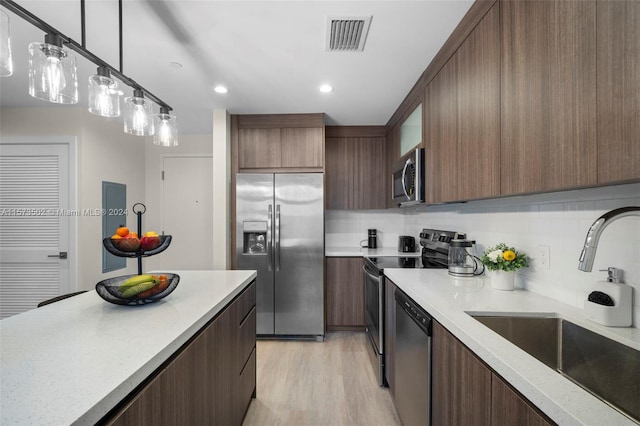 kitchen featuring decorative light fixtures, backsplash, stainless steel appliances, sink, and light hardwood / wood-style floors