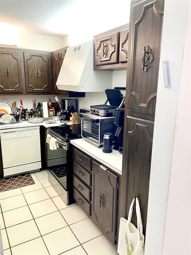 kitchen featuring stainless steel stove, custom range hood, dark brown cabinets, white dishwasher, and light tile floors