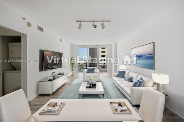 living area featuring visible vents, stacked washer / dryer, wood finished floors, rail lighting, and floor to ceiling windows