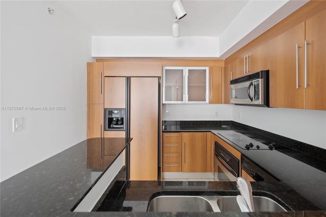 kitchen with stainless steel appliances, glass insert cabinets, a sink, dark stone countertops, and modern cabinets