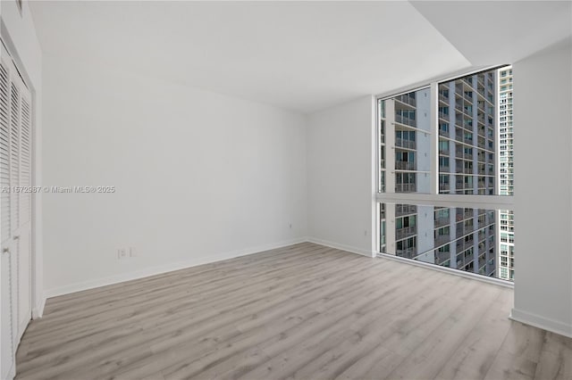 unfurnished room featuring expansive windows, wood finished floors, and baseboards