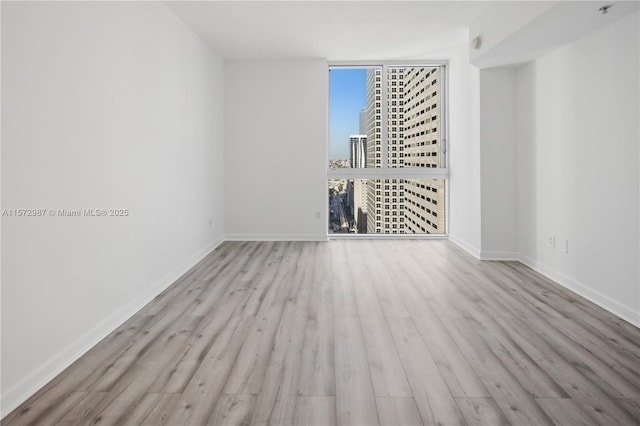 spare room featuring expansive windows, a view of city, baseboards, and wood finished floors