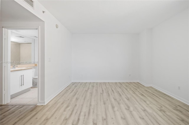 unfurnished room with light wood-style floors, visible vents, a sink, and baseboards