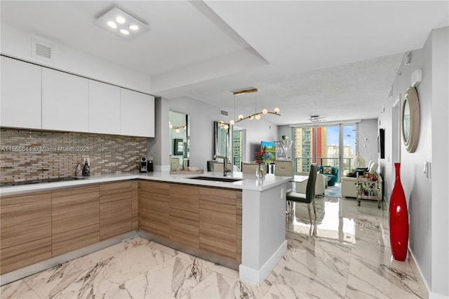 kitchen featuring white cabinetry, sink, hanging light fixtures, backsplash, and kitchen peninsula