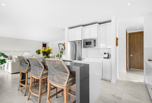 kitchen with a kitchen island with sink, white cabinets, appliances with stainless steel finishes, light tile floors, and a breakfast bar area